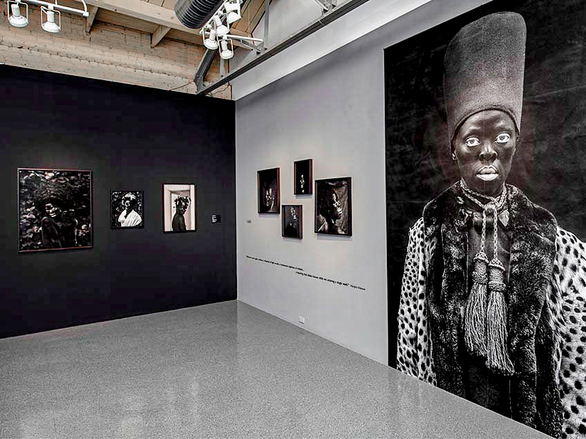 Art gallery interior with black-and-white photographic portraits on two-toned walls.
