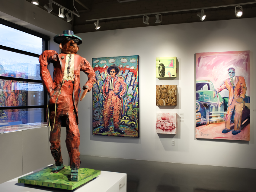 Gallery display featuring a colorful sculpture and paintings of stylized figures in suits.