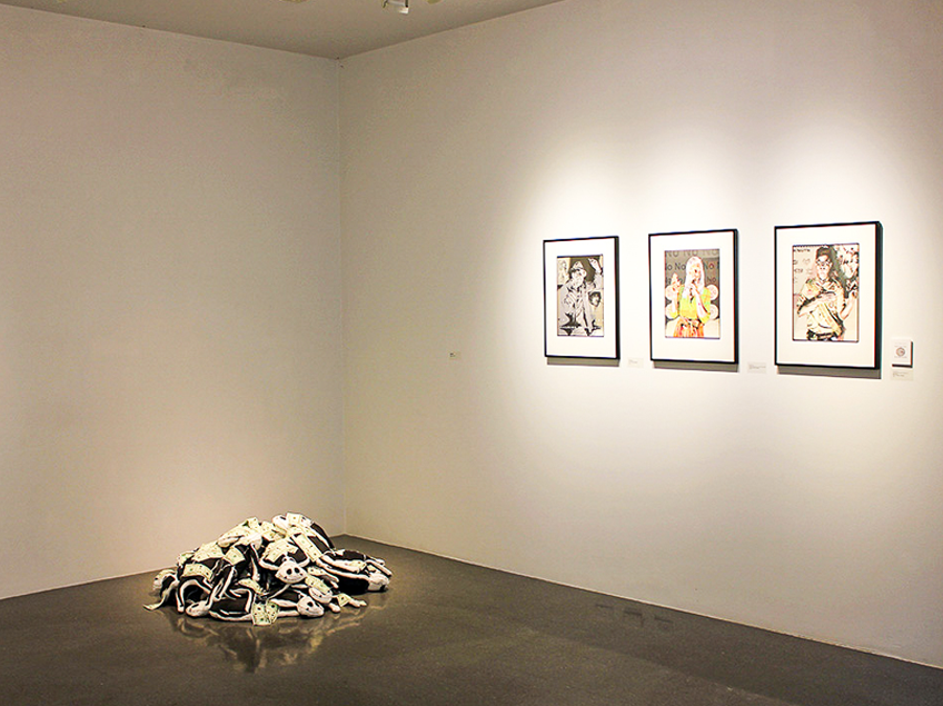 Art gallery corner with three framed artworks on a white wall and a pile of intertwined black and white sculptural elements on the floor.