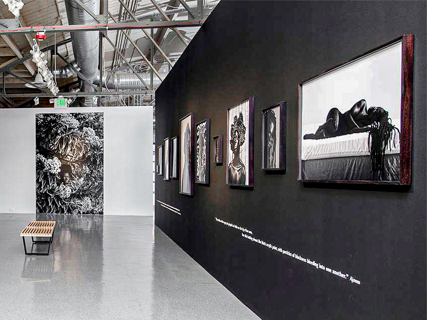 Art gallery with black and white photographs on black walls and a large central photo on a grey wall.