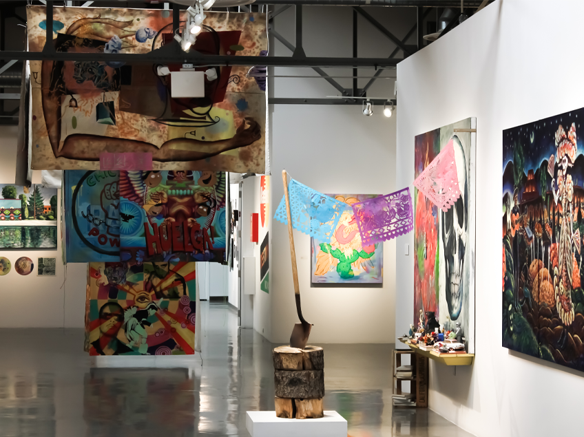 Contemporary art gallery with colorful abstract paintings, an shovel in a log, and papel picado decorations.