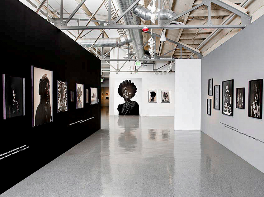 An art gallery with black and gray walls displaying framed photographs and a large central portrait.