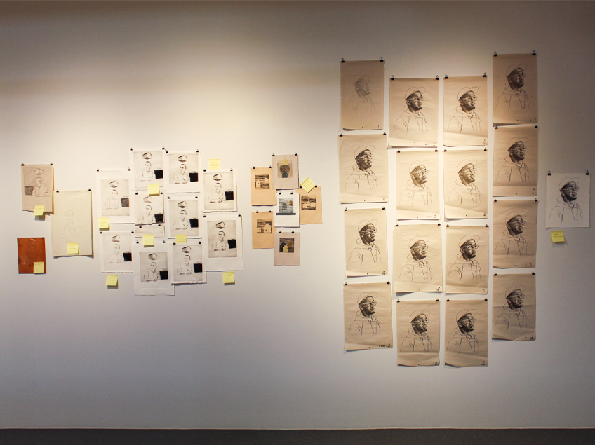 Wall with sketches and photos, including a grid of profile portraits on beige paper on a white wall.