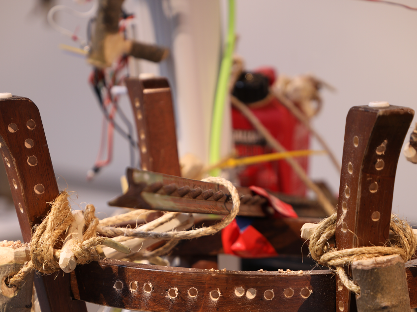 Close-up of wooden objects tied with ropes, part of an assemblage with a red container and colored wires.