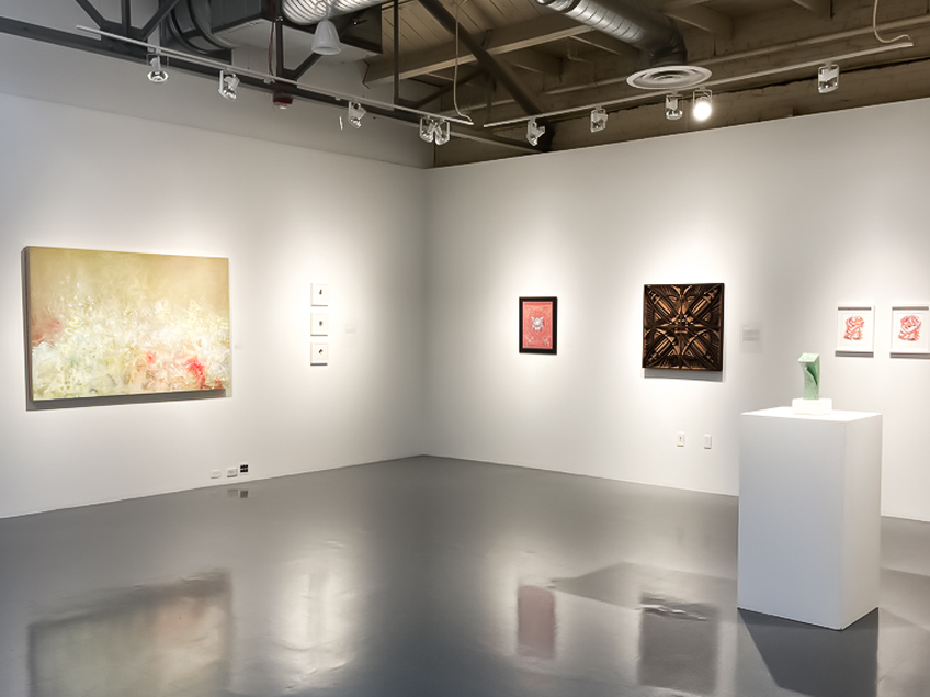 Contemporary art gallery with various abstract paintings and a sculpture on display.