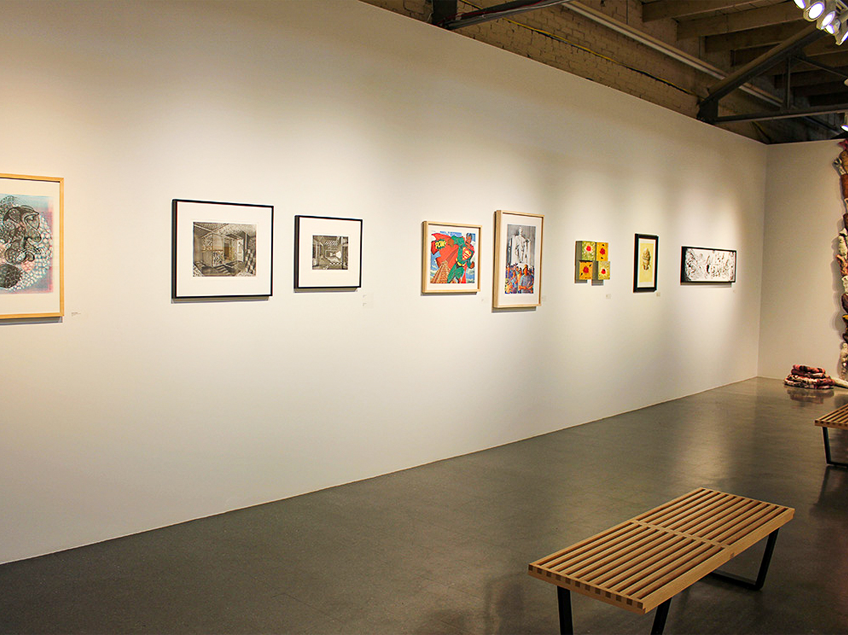 Art gallery with framed printed artworks on a white wall and wooden benches.