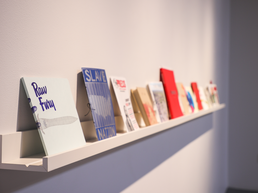 Books displayed upright on a minimalist wall-mounted shelf with varied cover designs and colors.