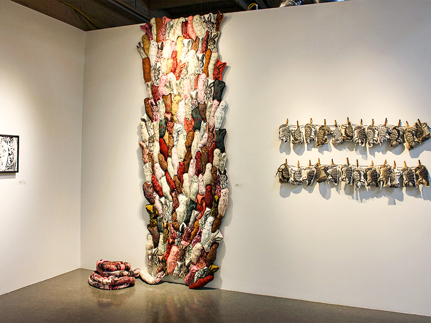 Art installation featuring colorful stuffed figures on a wall and two clotheslines with smaller animal figures.