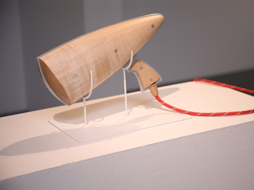 A wooden sculpture of a futuristic ray gun on a white pedestal with a red cord attached.