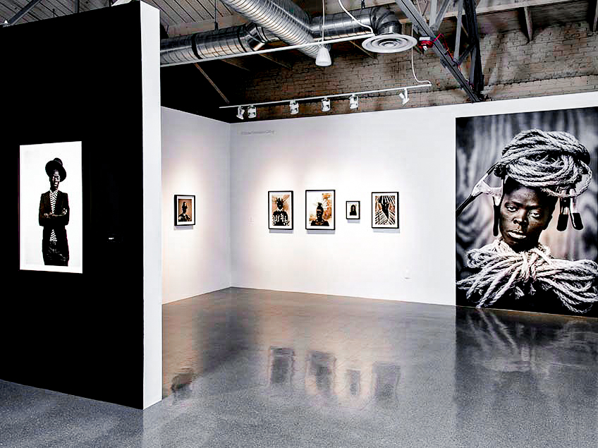 A modern art gallery with black-and-white portraits on white walls and an exposed industrial ceiling.