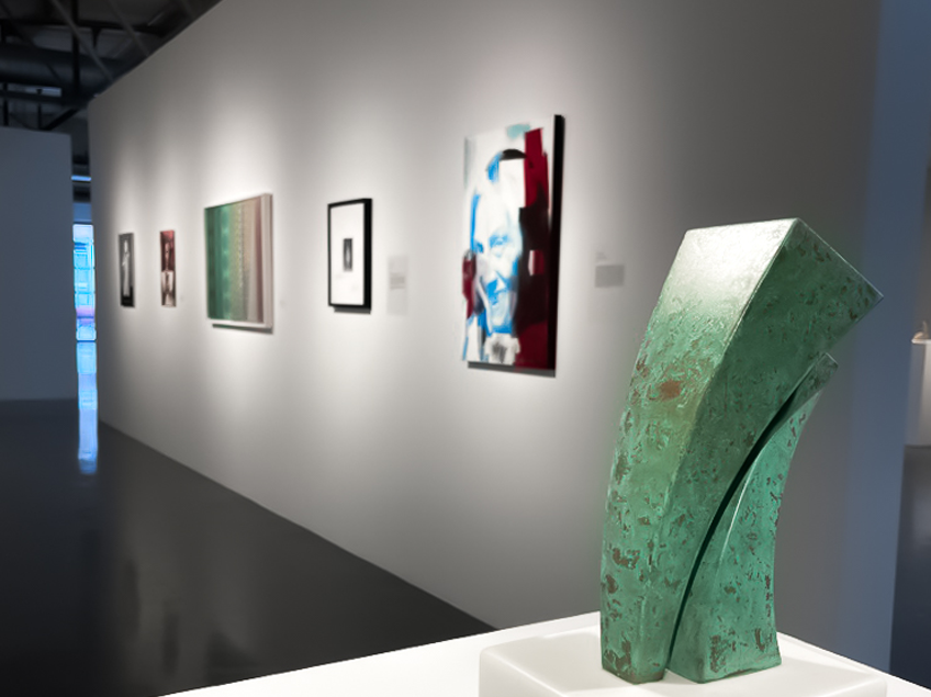 A modern art gallery featuring a green abstract sculpture with a curved design and multiple artworks on the wall.