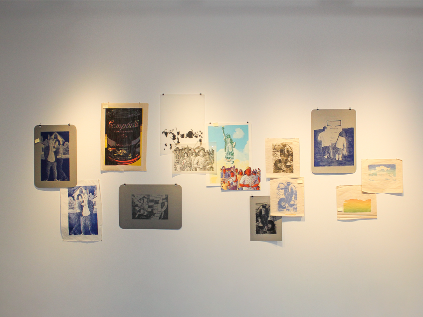 An art display on a white wall featuring twelve diverse artworks in various colors and styles.
