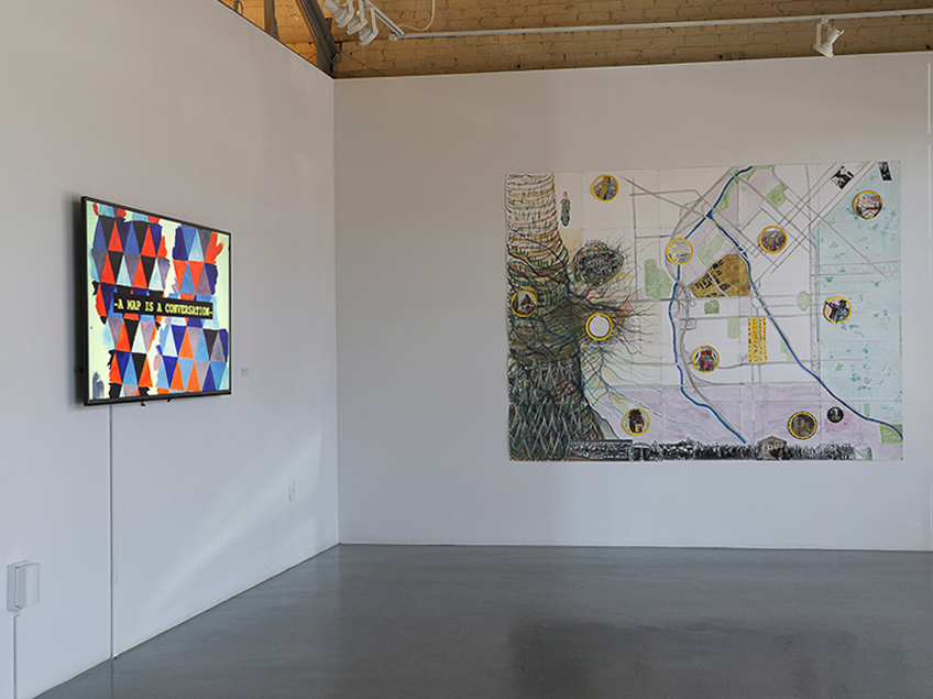 An art gallery with a digital screen and a large abstract artwork with a map theme on a white wall.