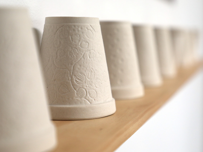 Row of white, embossed plaster flower pots on a wooden shelf.