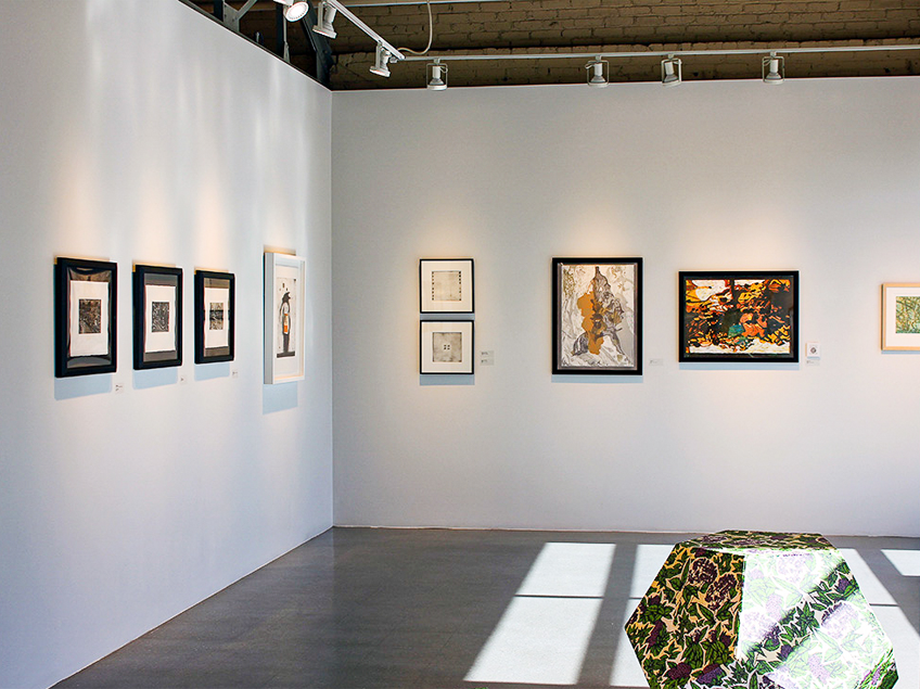 Art gallery interior with framed artworks on white walls and a colorful sculpture on the floor.