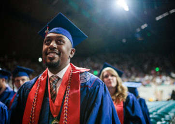 Male student in graduation regalia smiles