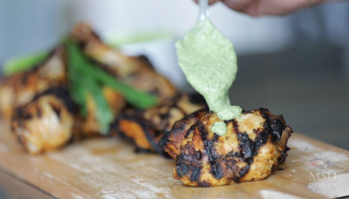 Close-up of cilantro sauce being spread over grilled chicken.