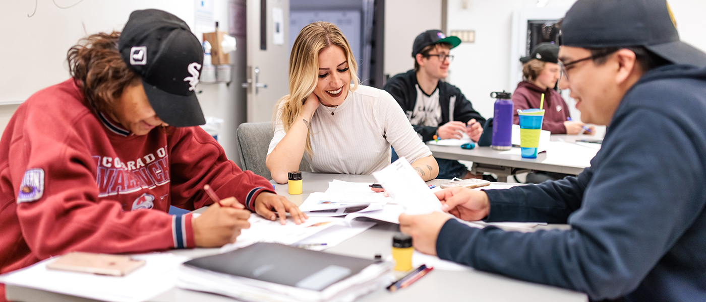 Three students sit at a table working together in a group, smiling at one another.