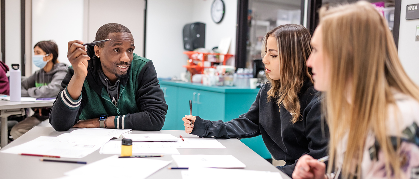 Three students sit at a table working together in a group.