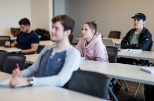 Four students at desks listening to lecture.