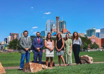 MSU Denver Corporate and Foundation Relations team standing in the grass in front of the Tivoli with downtown in the background