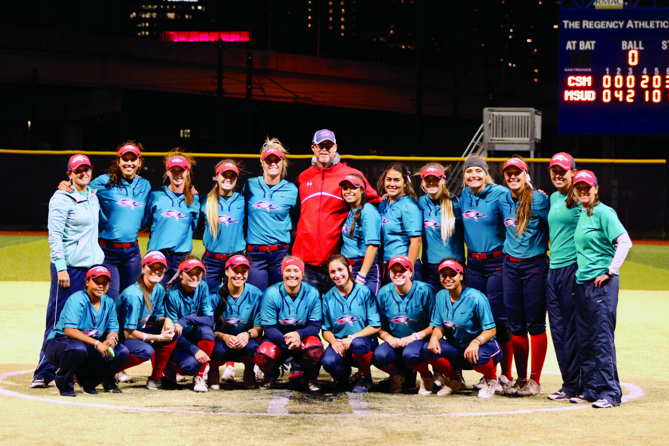 Jim Anderson standing with the softball team, wearing their teal jerseys for Strikeout Cancer