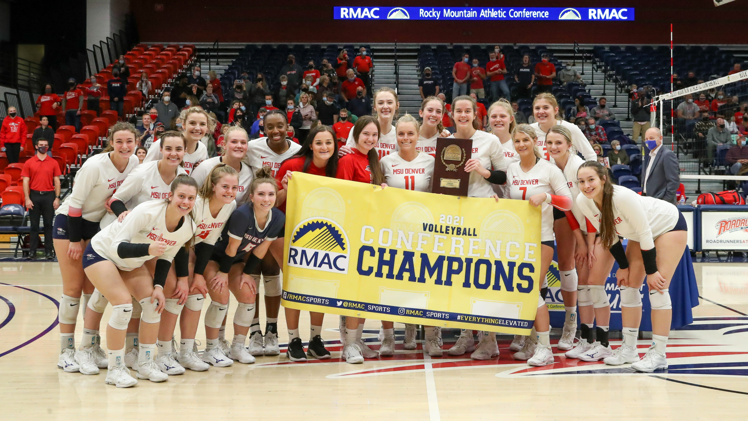 Roadrunners volleyball team celebrates the 2021 RMAC Championship with the banner.