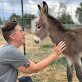 Claire Alfus laughing while petting a baby donkey