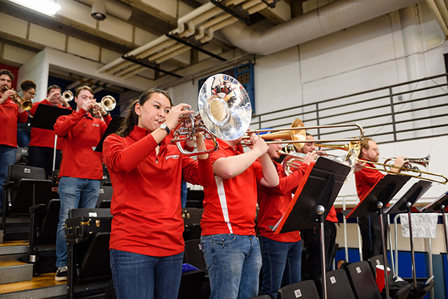 Mellophone player with shiny silver bell next to trombones at basketball game