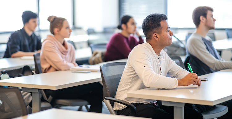 Five students sit at desks whilefocused on the front of the classroom.