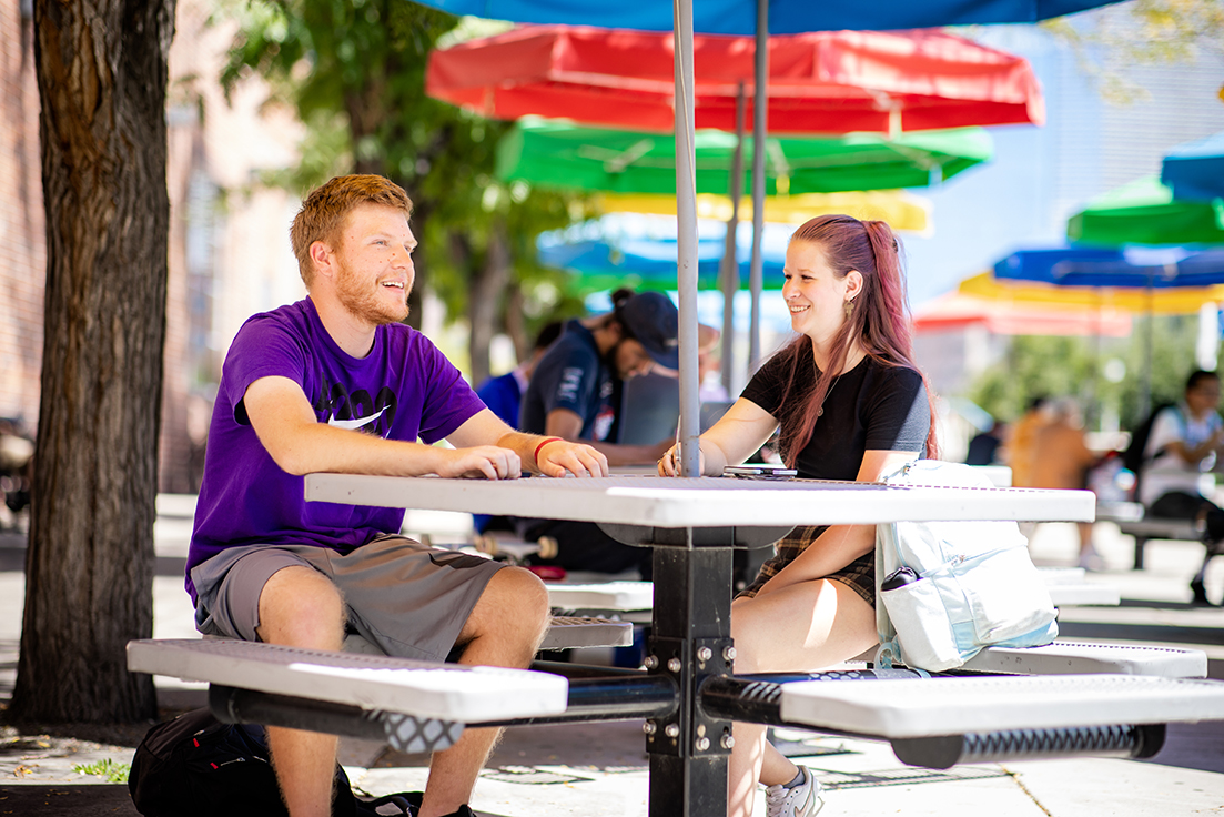 Two students sitting at an outdoor picnic table outside of the Tivoli