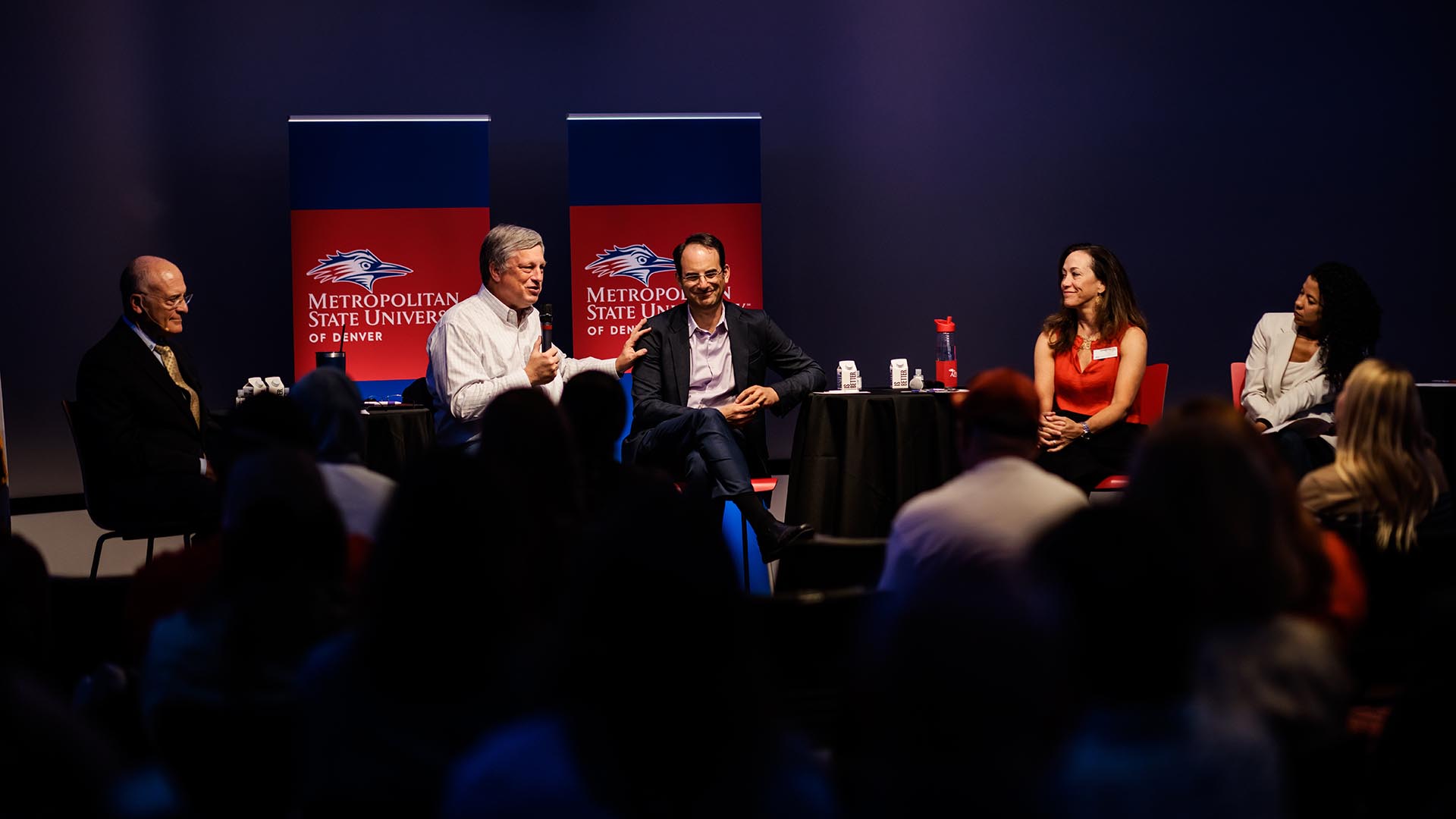 L to R, David Fine, Wayne Williams, Phil Weiser, Janine Davidson and Katia Campbell sitting on a panel in the CAVEA space on campus