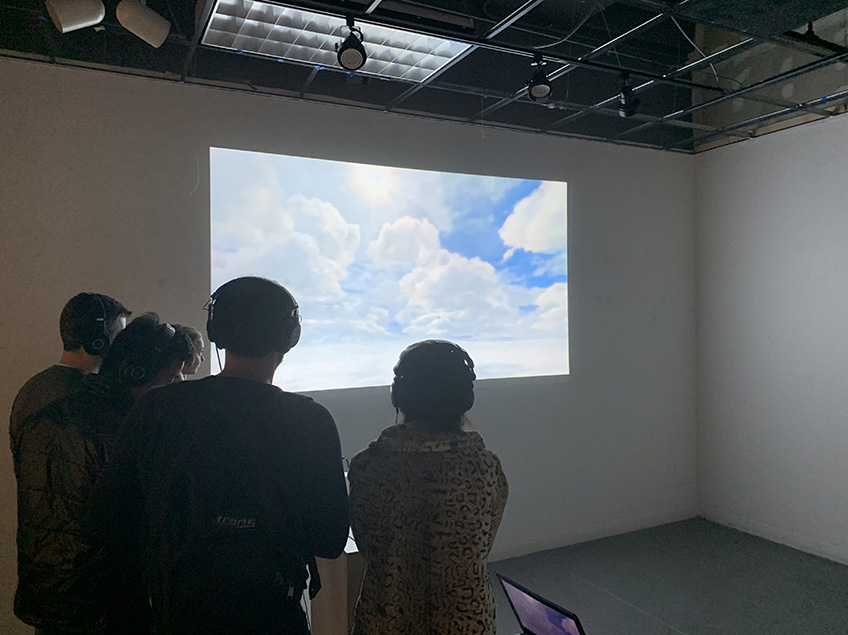 While wearing headphones, these four students are silhouetted against a projected image of the sky.