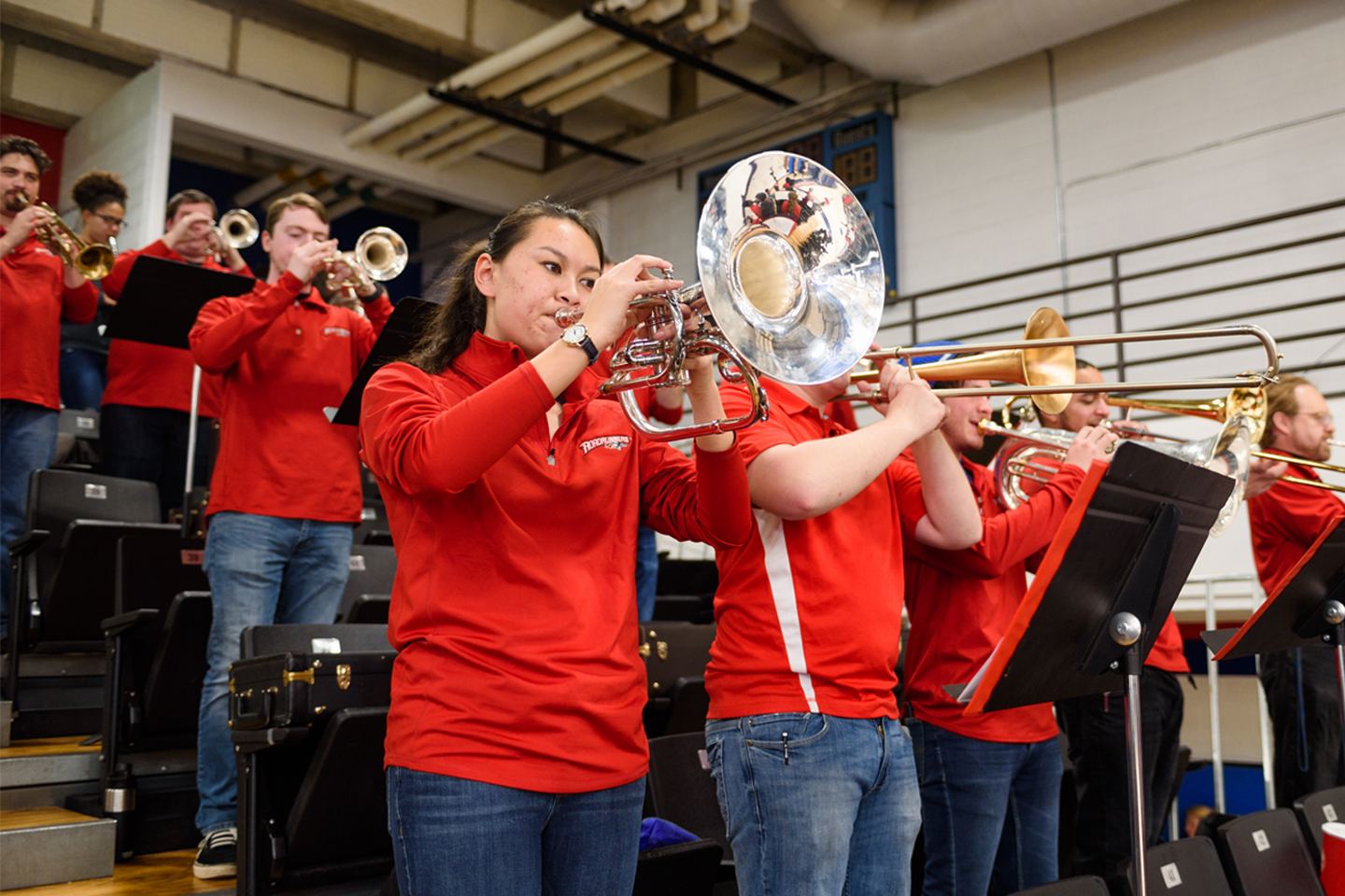 Group of pep band musicians in red playing in a basketball court