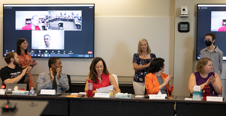 President Janine Davidson, Ph.D., sits while surrounded by cabinet members and Roadrunner shoutout winners in a talking shot.