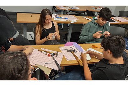 High school students working around a classroom table with design tools and paper.