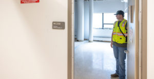 Man in neon construction vest stands in a doorway to the right to a classroom in the West building.