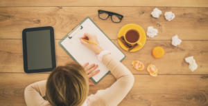 Overhead image of person working at a desk surrounded by tissues, tea and oranges.