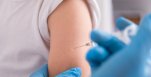 Closeup of person with blue gloves injecting a vaccine into a caucasian arm while no faces are in the photo.