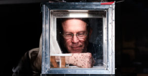 Bob Hancock, Ph.D., sticks his hand in glass box of mosquitos.