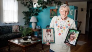 Eddy Reyes standing in his living room, holding photos of his late wife, Arlen Selu