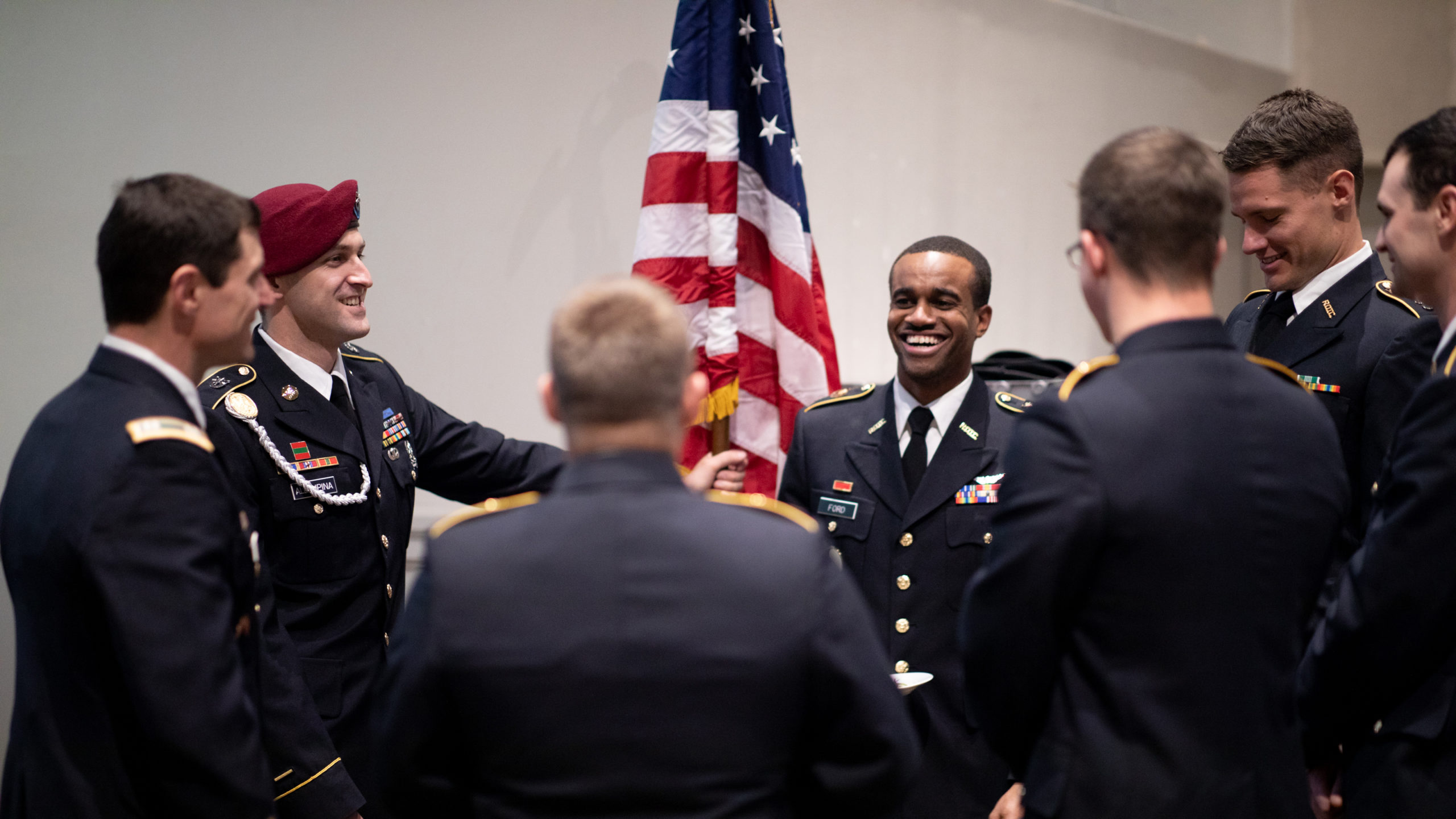 Veteran's Graduation, graduates dressed in military uniforms laughing in front of an American flag