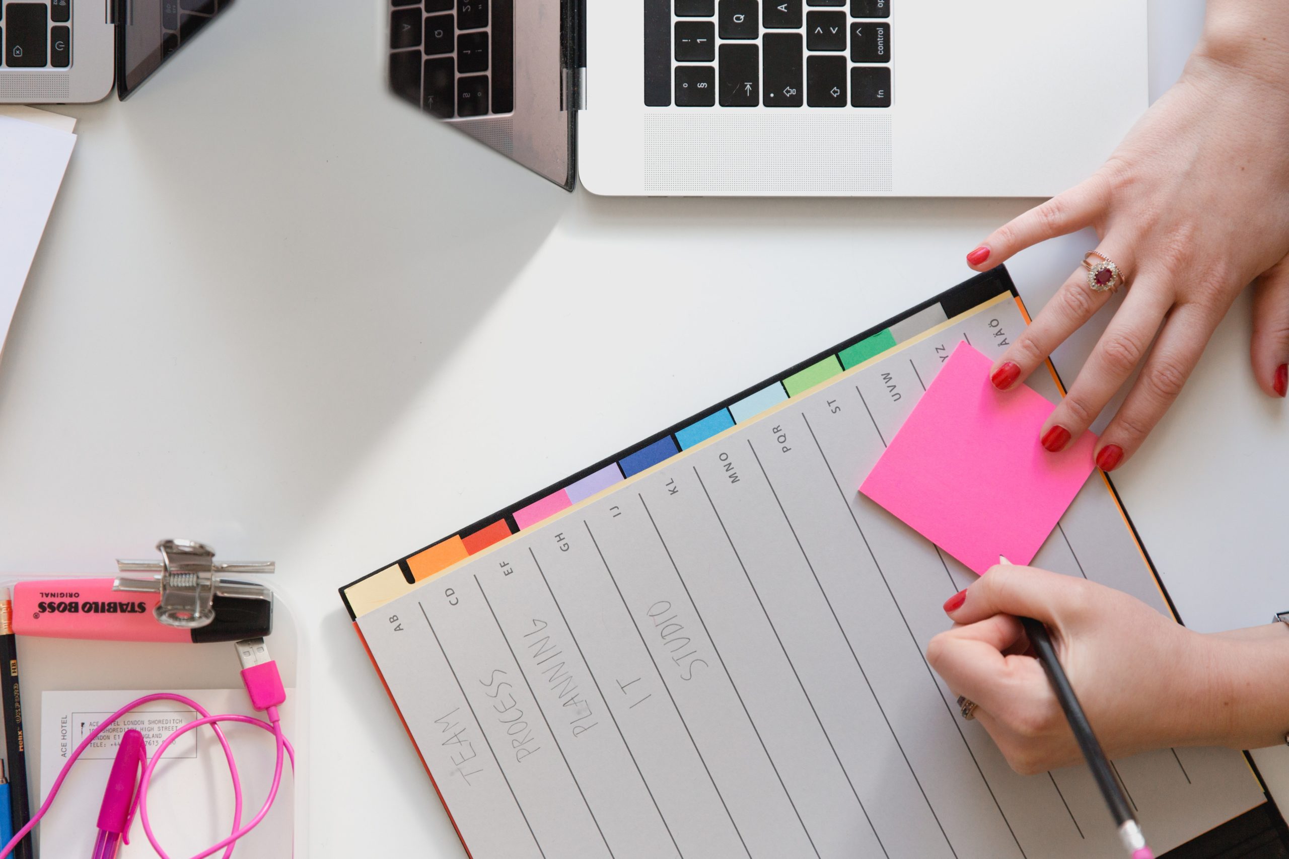 Person holding a pencil writing on pink sticky note