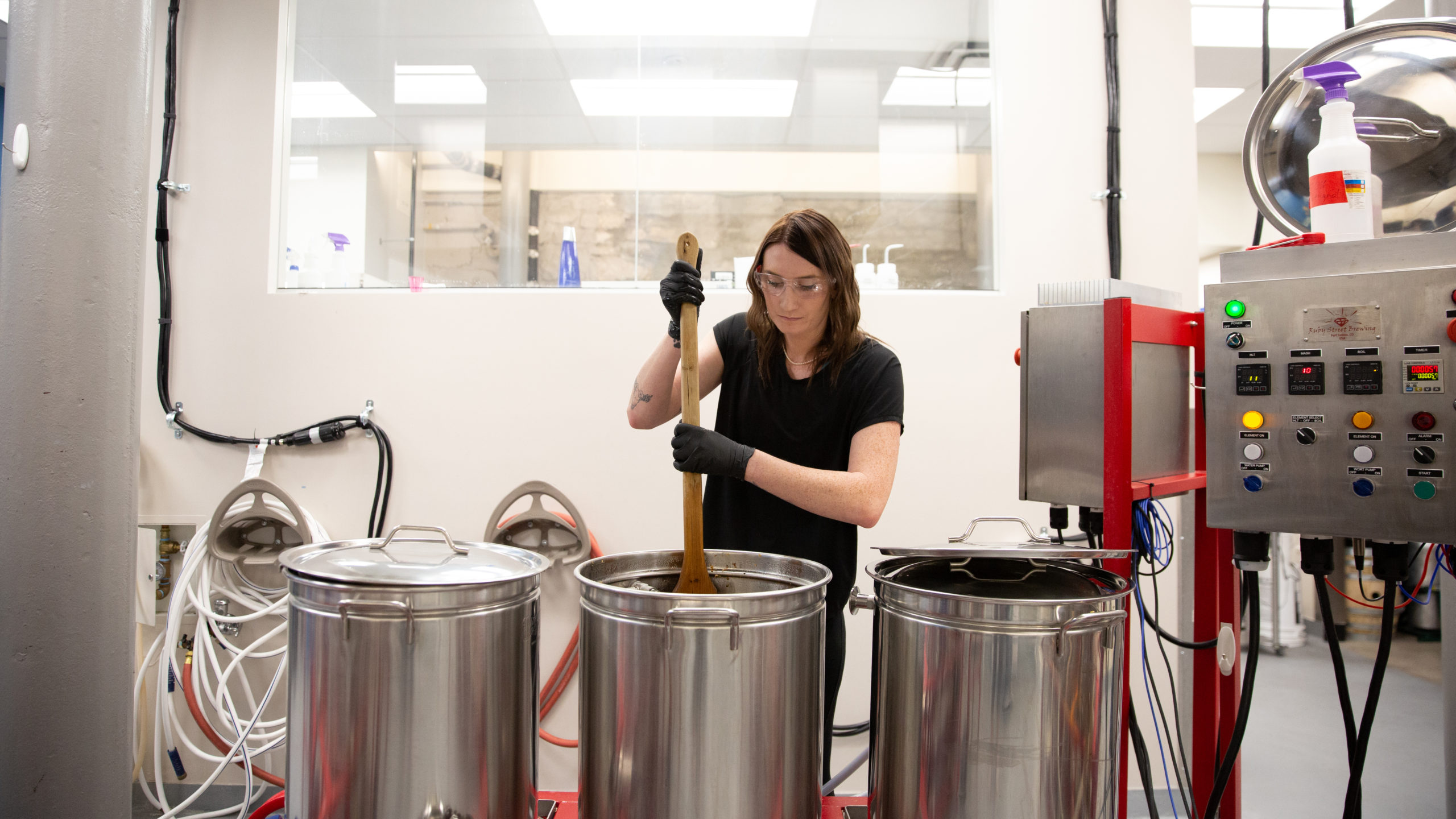 A female student stirring a giant pot in a brewery in the beer-making process.