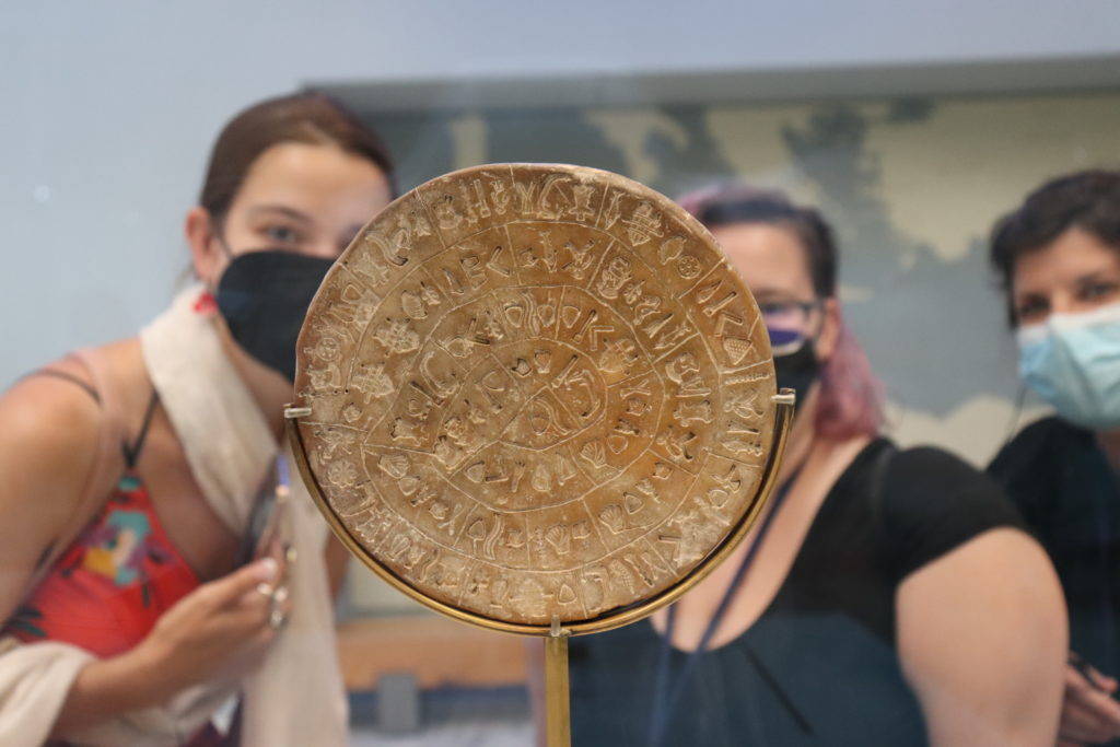 Students in the background regard a circular stone with ancient writing.