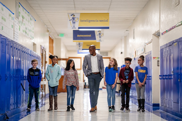 Elementary-school students walking alongside a teacher in the school's hallway.