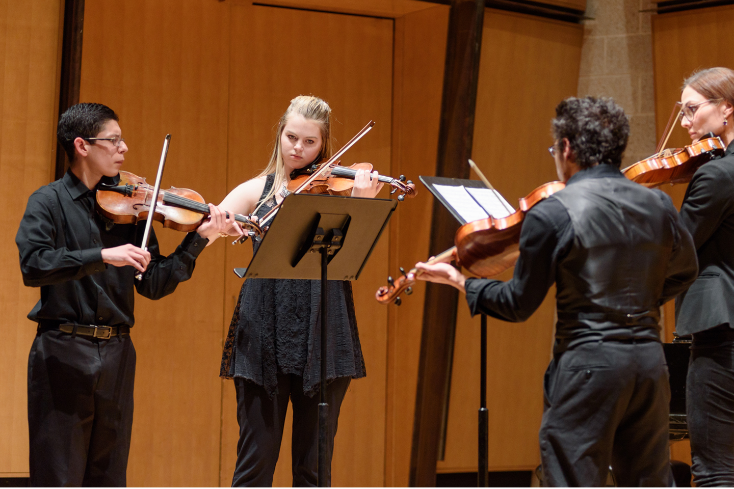Three violinist and a violist perform on a stage