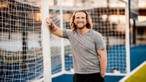 Jamie Farmer, smiling and leaning with his right arm against a soccer goalpost.