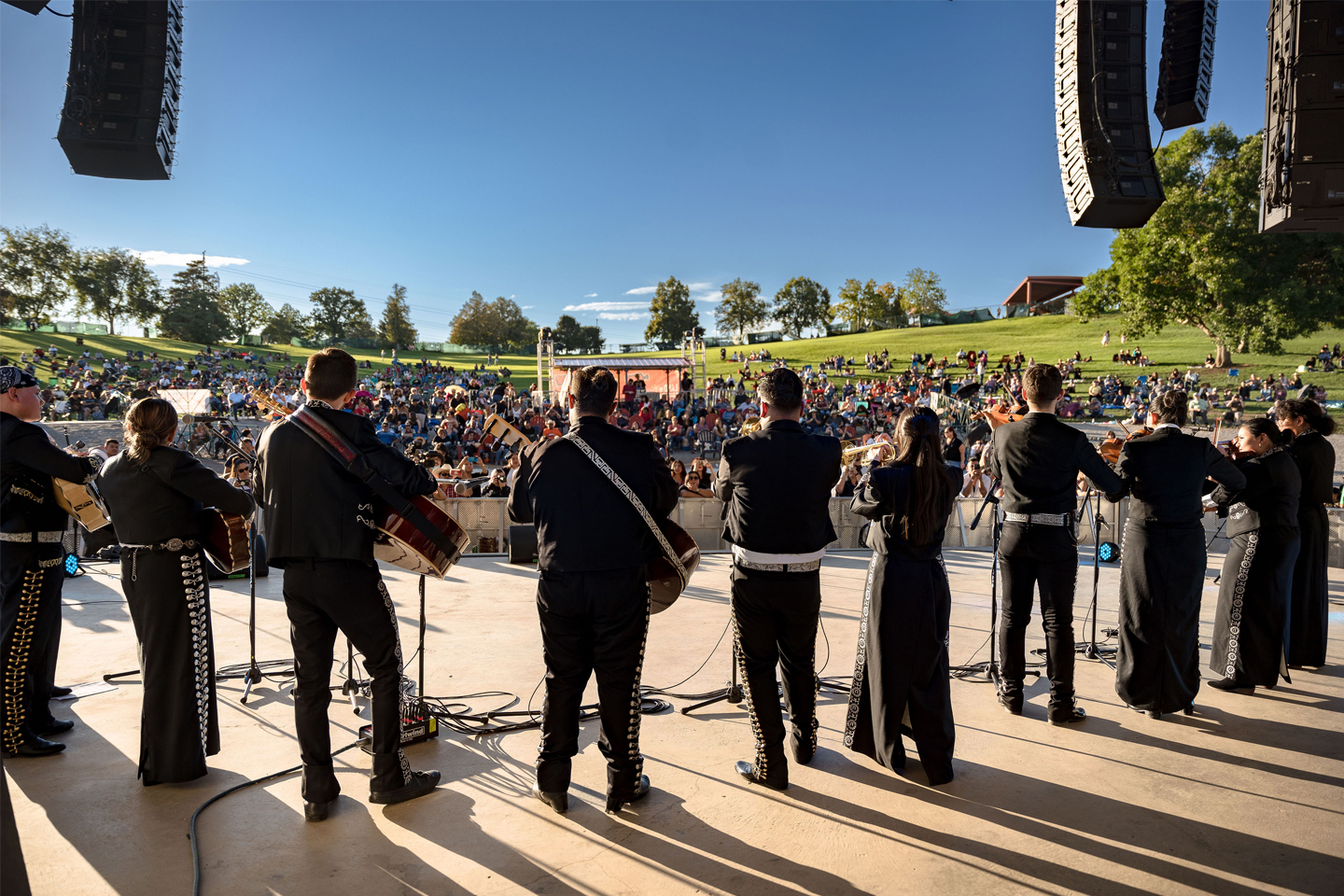 Mariachi group standing on outdoor stage before crowd