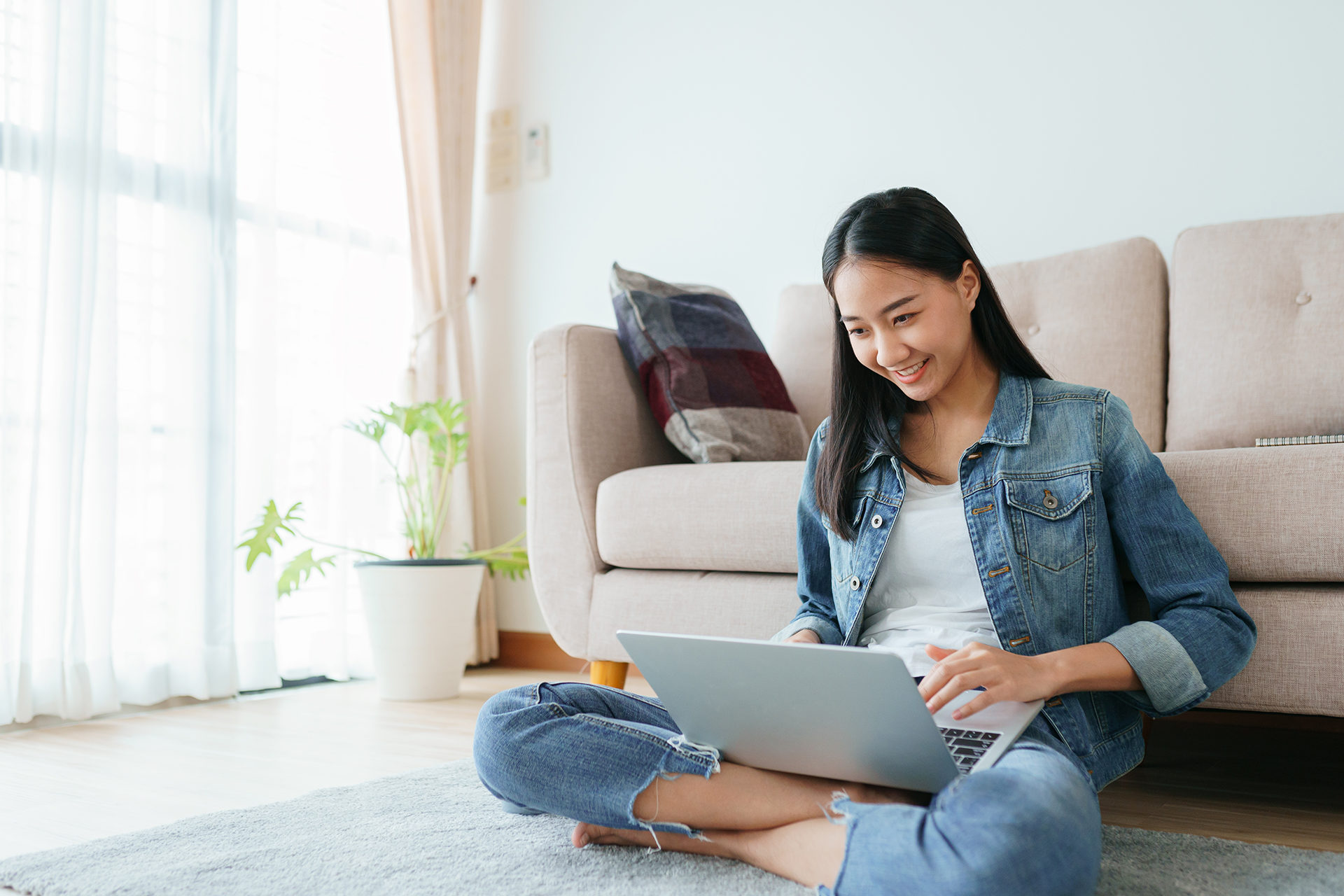 Asian girl wearing jeans using a laptop while sitting on the floor at home. Freelance girls are video conferencing with colleagues on social media. concepts work from home and new normal